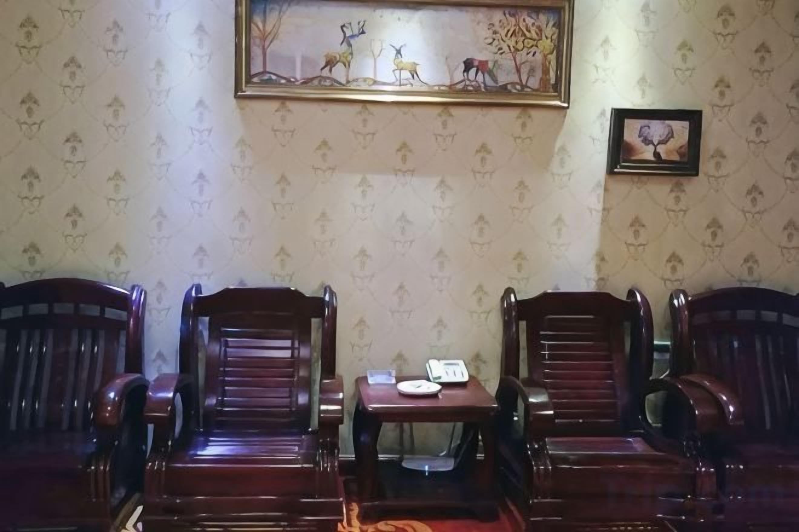 A room with three wooden chairs, a small table with a phone and a notepad, and patterned wallpaper.