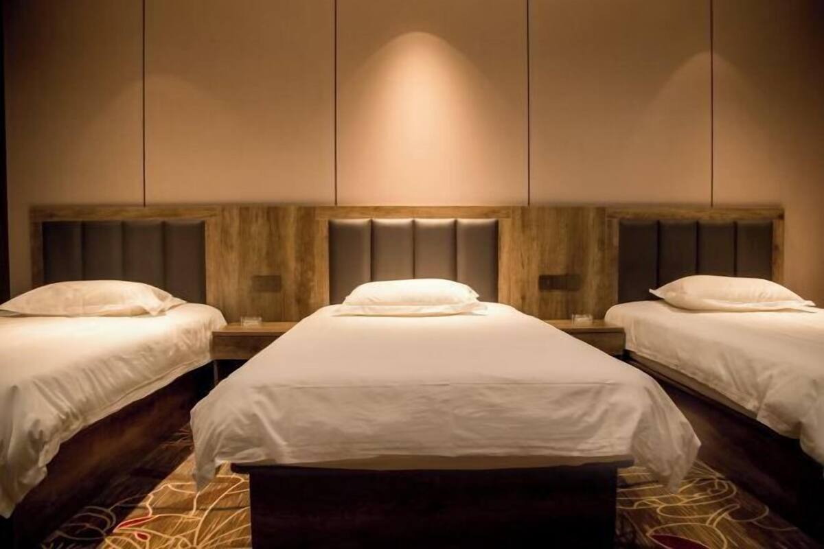 A hotel room with three beds, wooden headboards, and a patterned carpet.