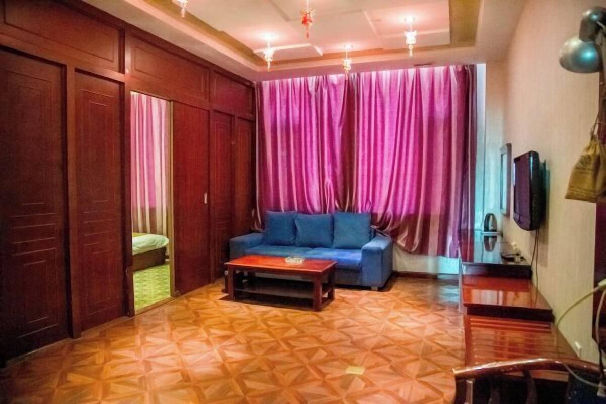 A room with a patterned floor, a blue sofa, a wooden coffee table, and a TV on the wall.