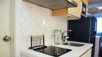 Una cocina con baldosas blancas tipo espiga, una placa de inducción negra, un lavamanos de acero inoxidable y armarios de madera.