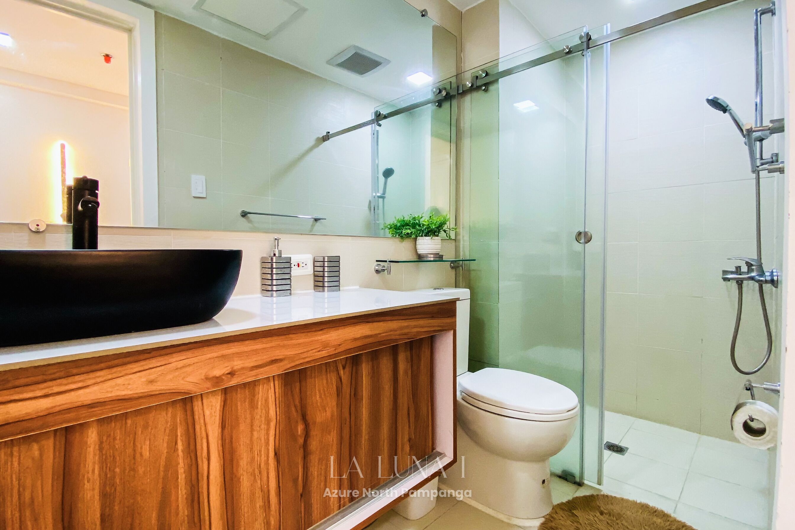 Ein modernes Badezimmer mit einem Holzkosmetikschrank, einem großen Spiegel, einer Glasdusche und einer Toilette.