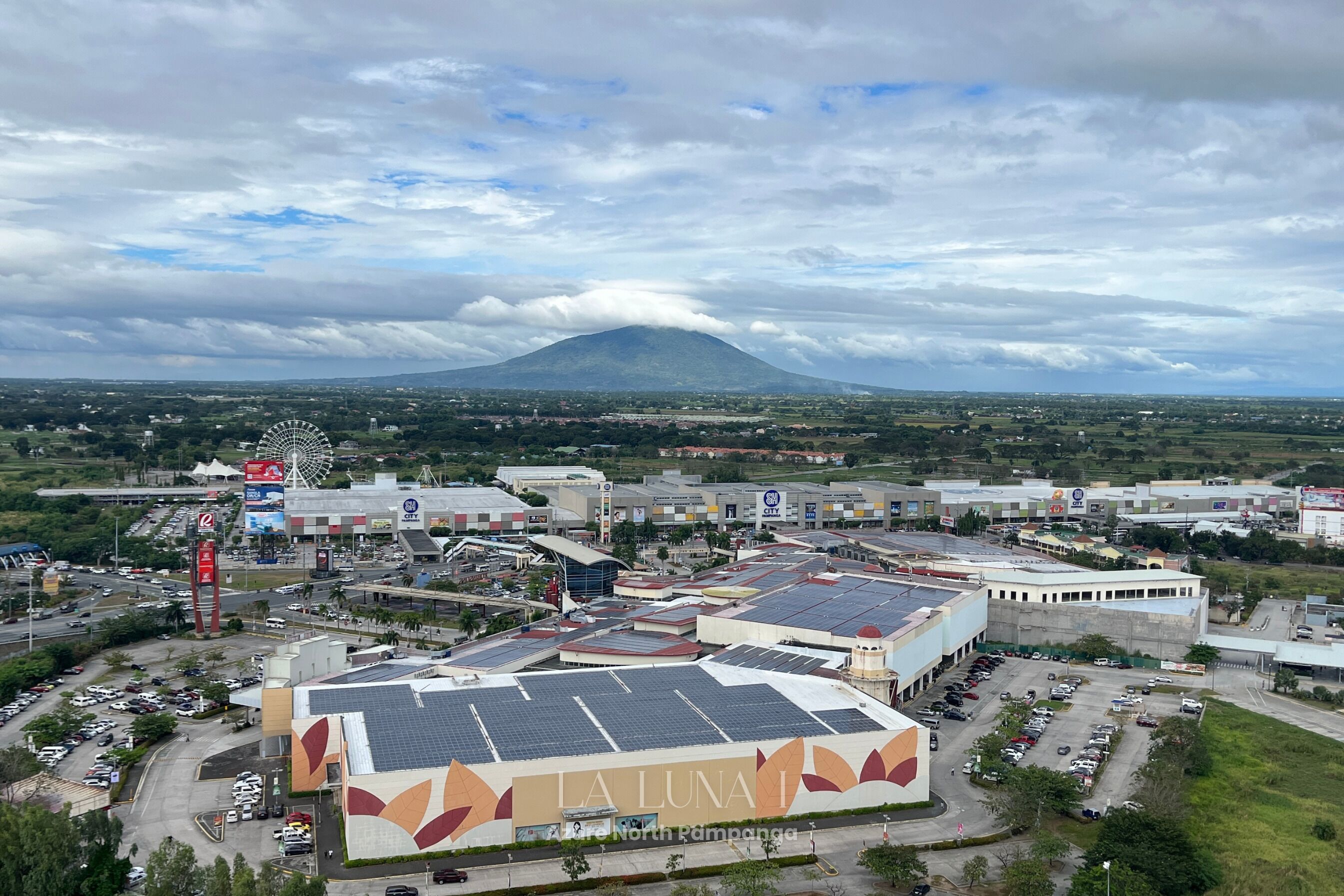 A large commercial building with solar panels, a Ferris wheel, and a mountain in the background.