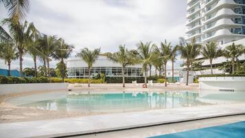 A pool area with palm trees, a modern building, and a clear sky.