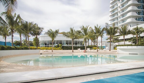 A pool area with palm trees, a modern building, and a clear sky.