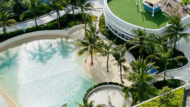 An aerial view of a resort with a large pool, palm trees, and a circular building with a green roof. - Solei Oak: Pet Friendly Studio with Netflix, Boardgames, Beach & Mt. Arayat View (San Fernando)