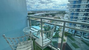 A balcony with a glass table and chair, overlooking a cityscape with buildings and greenery. - Solei Oak: Pet Friendly Studio with Netflix, Boardgames, Beach & Mt. Arayat View (San Fernando)