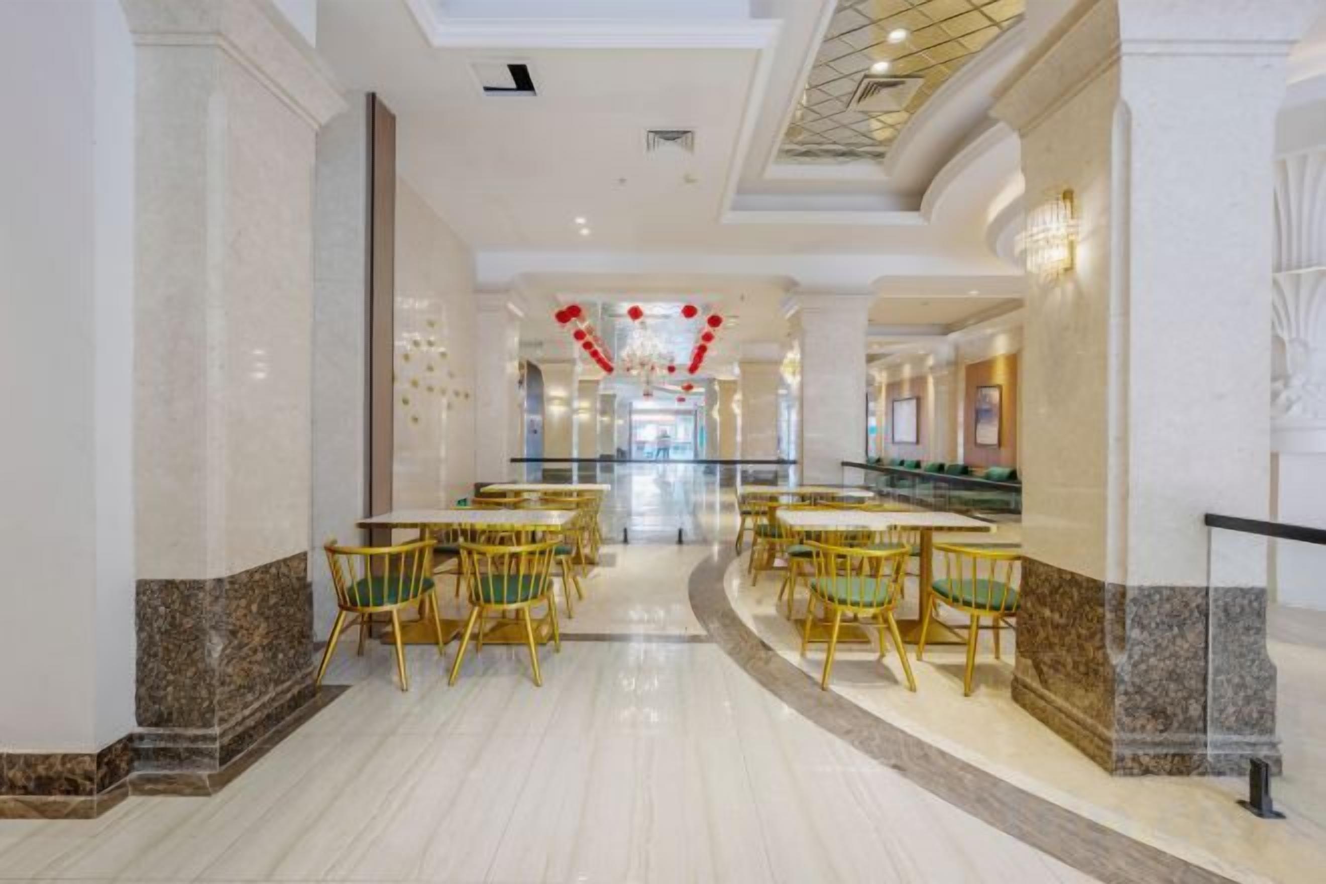 A hotel lobby with a marble floor, round tables, and green chairs.