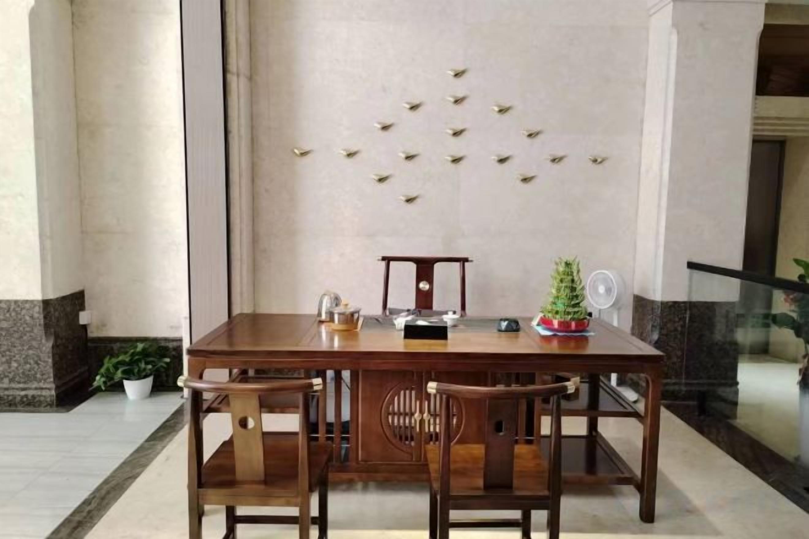 A wooden dining table with chairs, a small Christmas tree, and a decorative wall with golden elements.