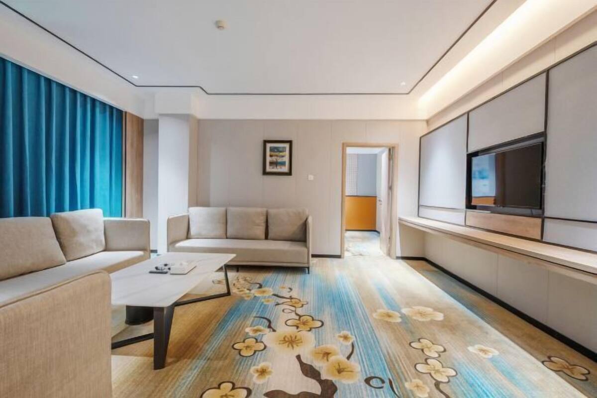 Une chambre d’hôtel moderne, dotée d’un canapé, d’une table basse, d’un téléviseur et d’une moquette à motifs floraux.