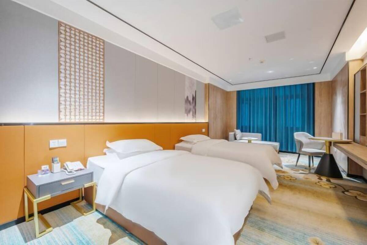 Une chambre d’hôtel avec deux lits, un bureau, une chaise et une grande fenêtre avec des rideaux.