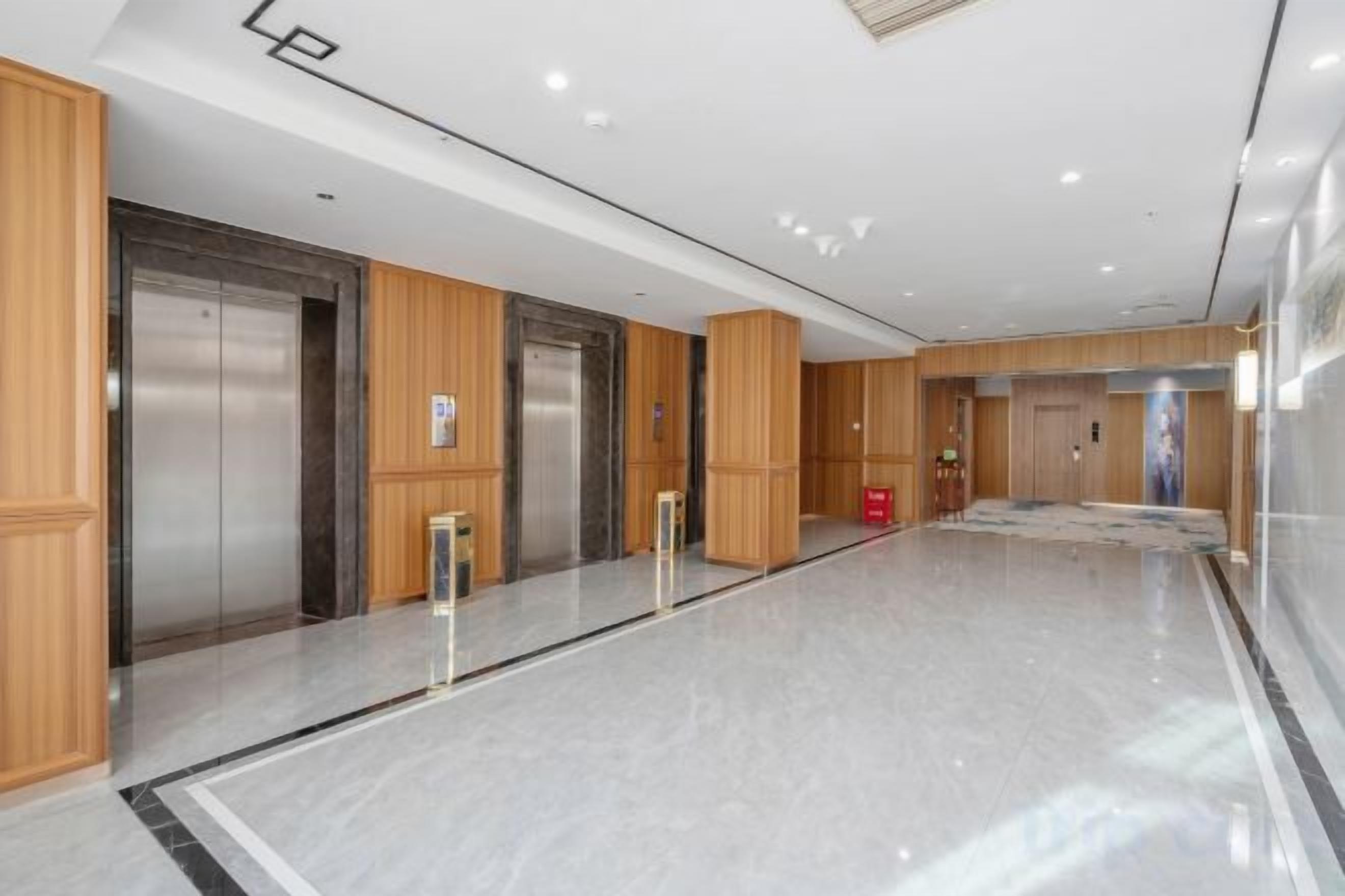 A modern hotel lobby with elevators, a reception desk, and a marble floor.