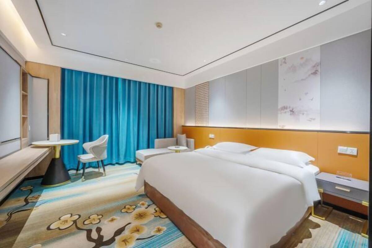 Une chambre d’hôtel avec un lit, un bureau, une chaise et un rideau bleu.