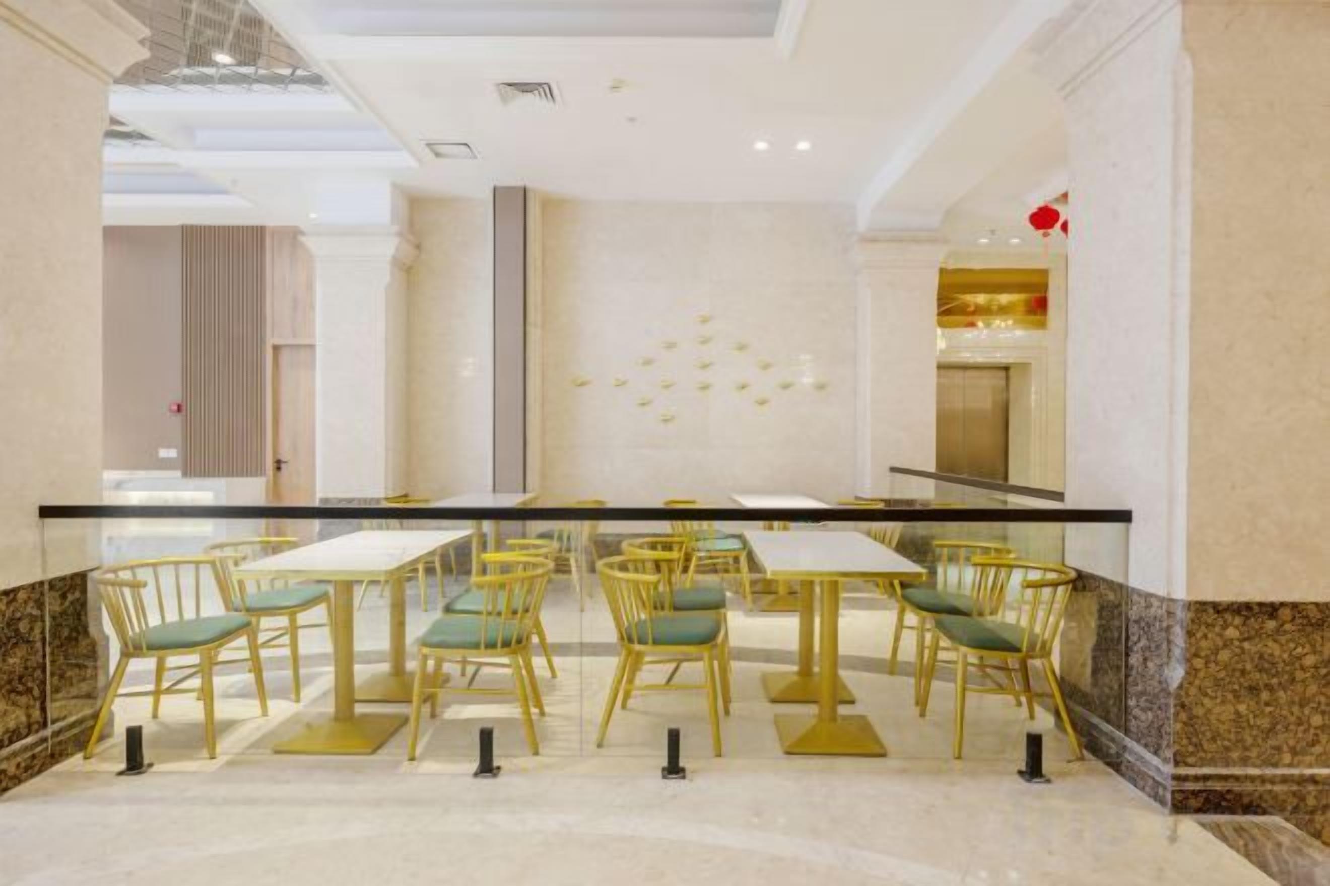 Un vestíbulo de hotel con suelo de mármol, barandilla de cristal y una fila de mesas y sillas.