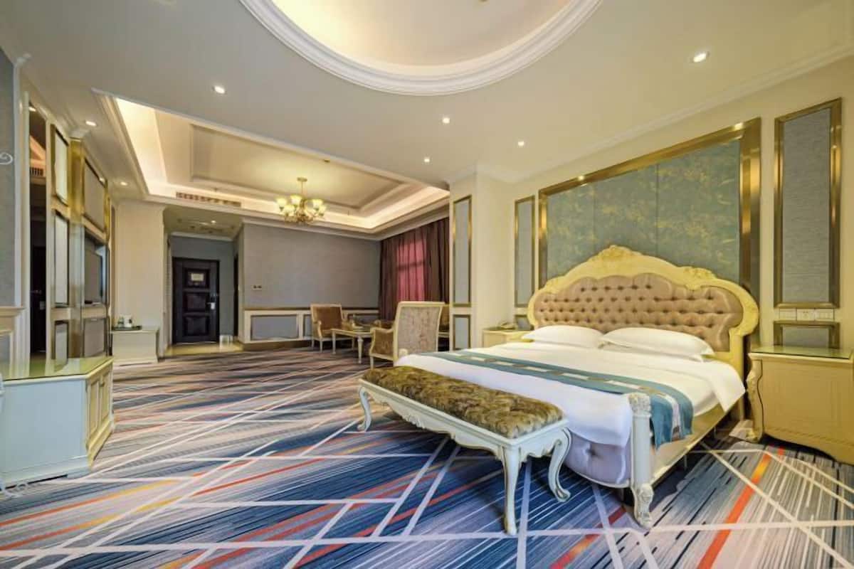 Une chambre d’hôtel spacieuse, dotée d’un grand lit, d’une banquette, d’un bureau et d’un miroir.