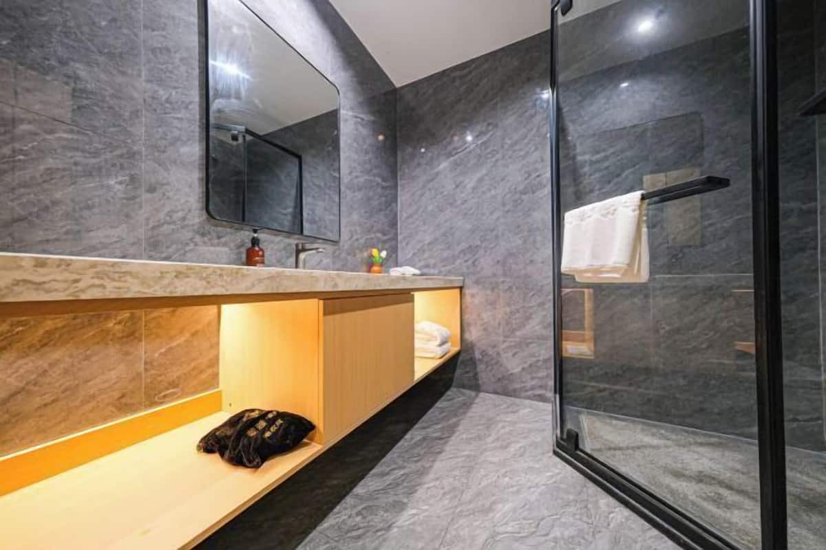 Une salle de bain moderne avec un mur en marbre, une cabine de douche en verre et un meuble-lavabo en bois.
