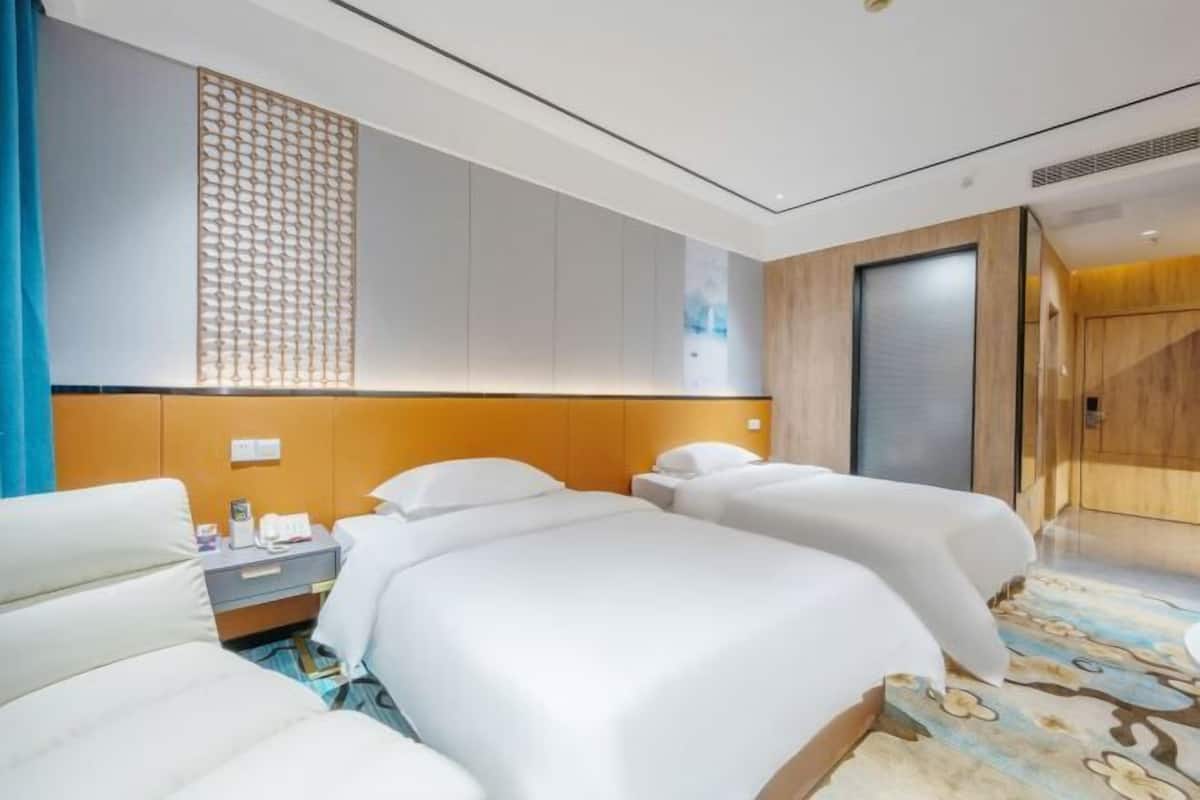 Une chambre d’hôtel avec deux lits, un bureau, une chaise, un panneau décoratif au mur et une porte en bois.