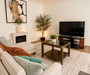 A living room with a sofa, a glass coffee table, a TV, a fireplace, and a potted plant.