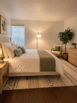 A bedroom with a bed, bedside table, lamp, chair, dresser, and a large plant.