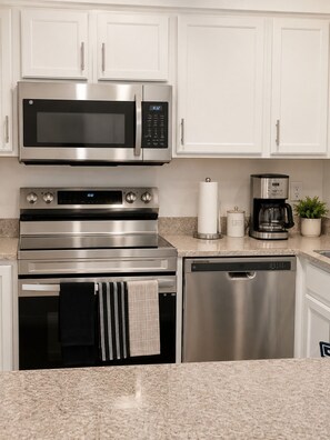 A kitchen with a stainless steel microwave, oven, and dishwasher, white cabinets, and a coffee maker. - Living at the Palms (Tarpon Springs)