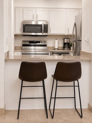 A kitchen with white cabinets, stainless steel appliances, and two bar stools.