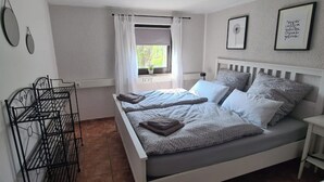 A bedroom with a bed, a window with curtains, a bedside table, and wall decorations. - Gemütliche Ferienwohnung im Bergischen - Nähe Köln/bonn Haustierfreundlich! (Much)