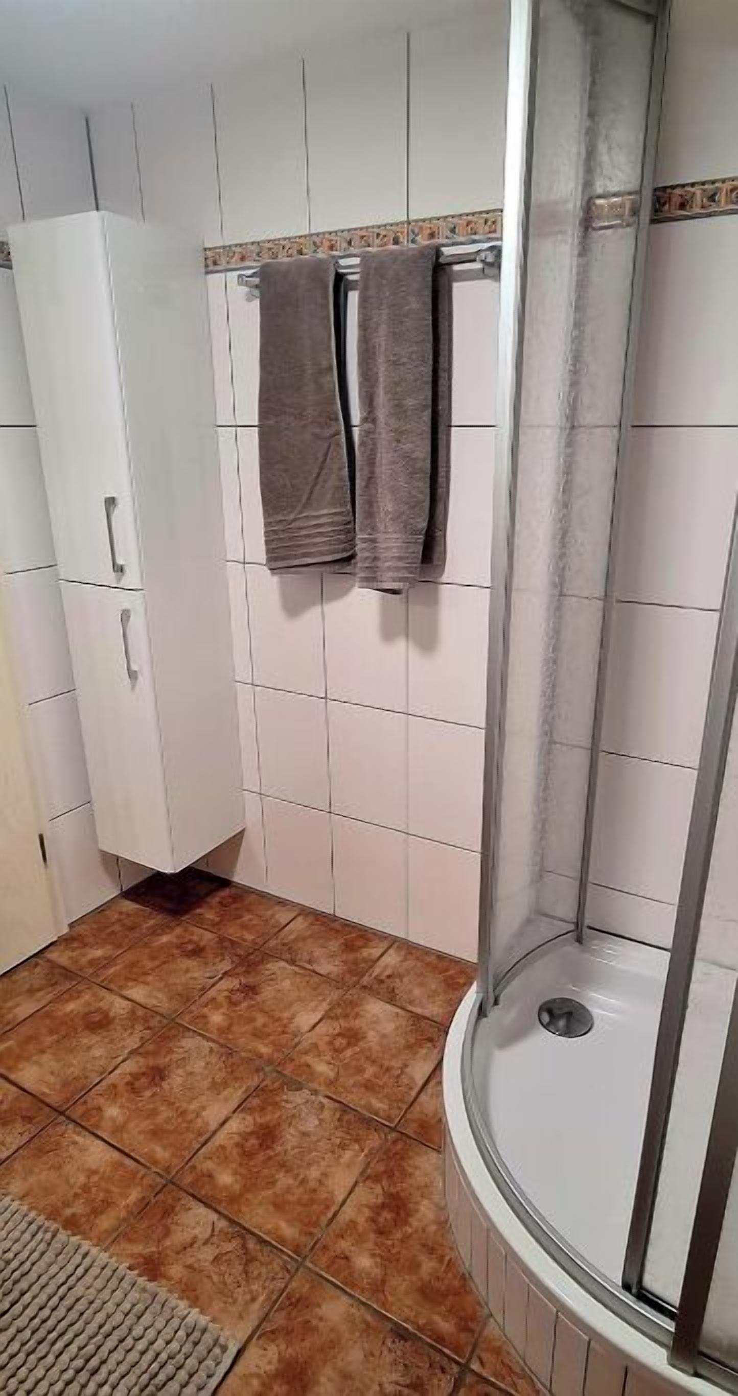 Un baño con ducha, paredes de azulejos, un armario blanco y dos toallas colgadas.