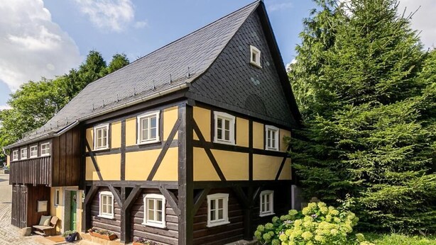 Una casa tradicional con entramado de madera y techo pronunciado, vigas de madera y una ventana pequeña.