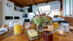 Una mesa de desayuno con jugo de naranja, mantequilla, mermelada y un florero con flores.