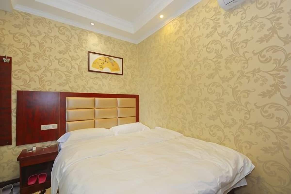 A hotel room with a bed, a wooden headboard, a nightstand, and a wall-mounted air conditioner.