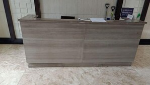 A reception desk with a light wood finish, a tiled floor, and a wall with a geometric pattern. - Zhengzhou Wanyinli Hotel (Zhengzhou)