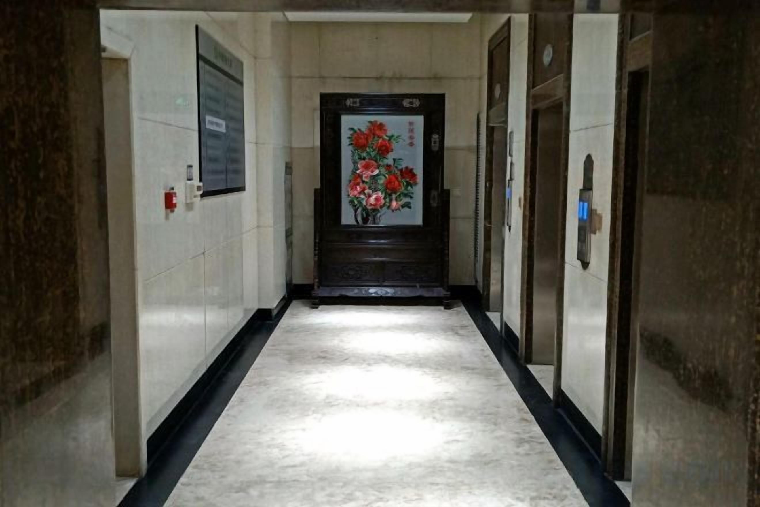 A hallway with a marble floor, a door with a floral painting, and two elevators.