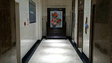 A hallway with a marble floor, a door with a floral painting, and two elevators.