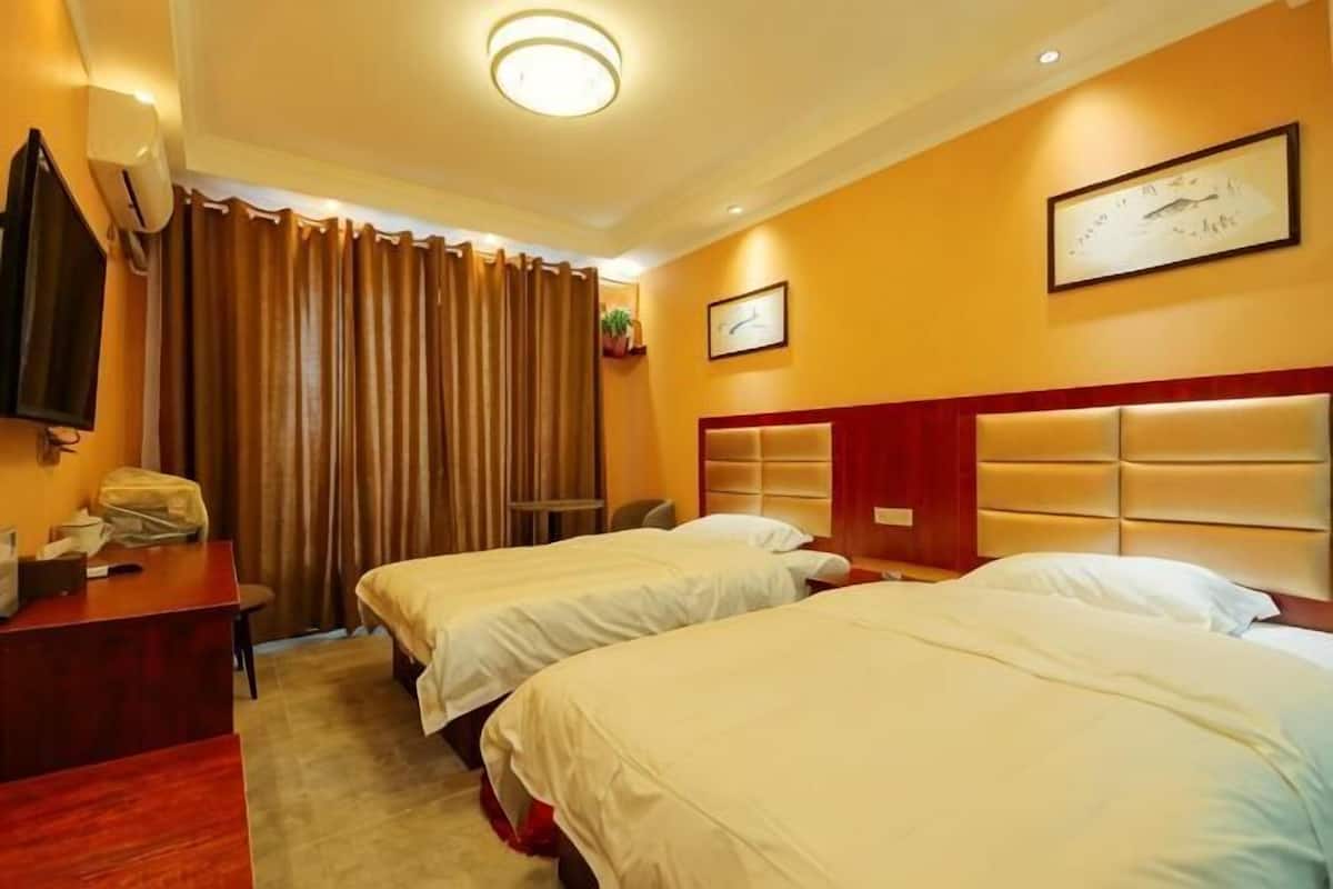 A hotel room with two beds, a desk, a chair, a TV, and a clock on the wall.