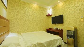 Quarto de hotel com cama, televisão, frigobar e prateleira fixada na parede.
