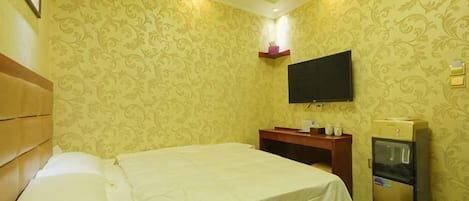 Ett hotellrum med en säng, en tv, en minibar och en hylla som är monterad på väggen.
