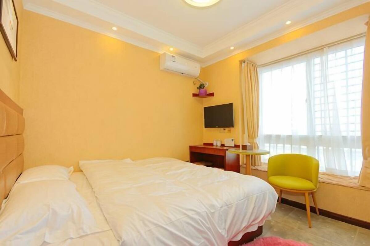 A hotel room with a bed, a TV, a chair, and a window with curtains.
