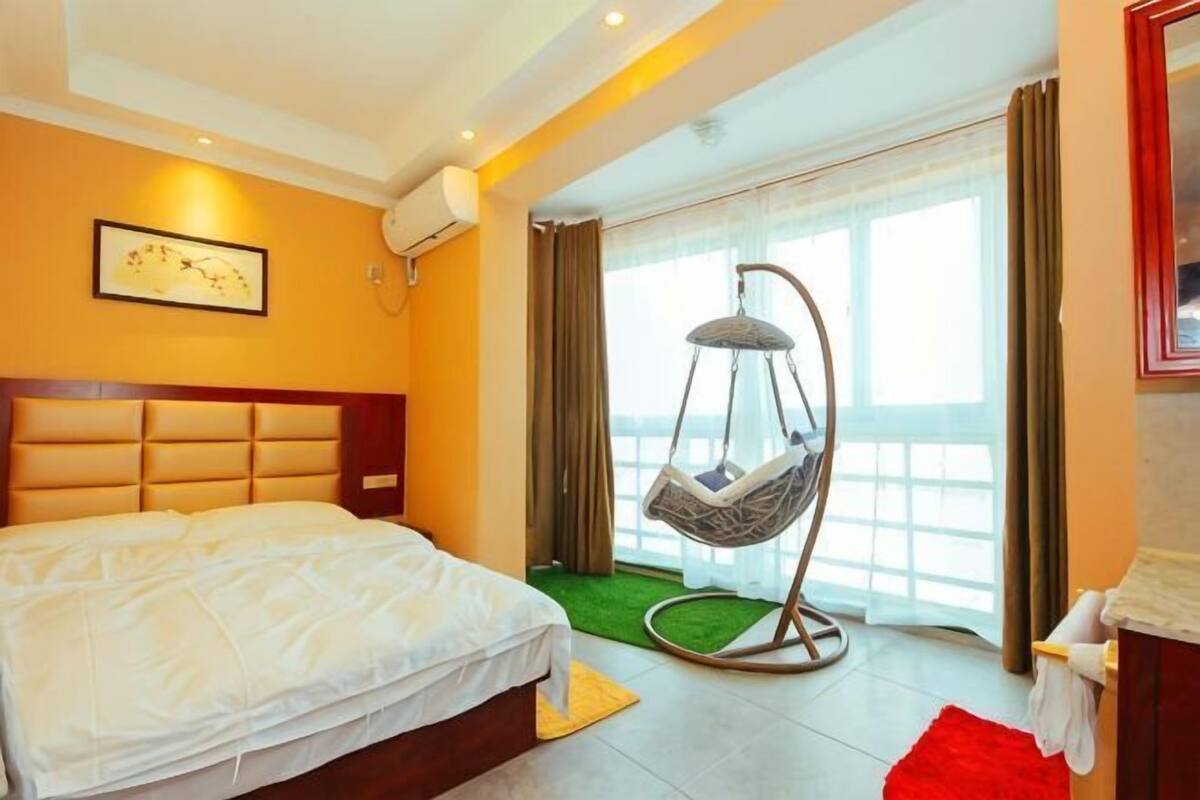 A hotel room with a bed, a hanging chair, a window with curtains, and a view of the outside.