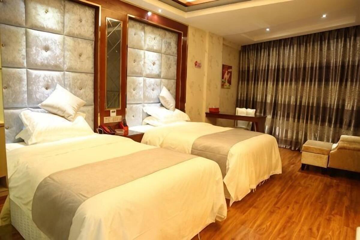 Une chambre d’hôtel avec deux lits, un plancher en bois, un grand miroir et un rideau.