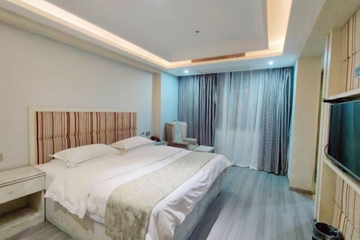A hotel room with a bed, bedside table, chair, curtains, and a TV.