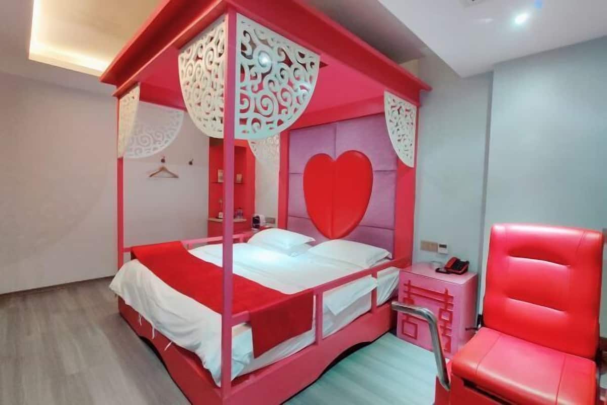 Un lit à baldaquin avec une tête de lit en forme de cœur, une chaise rouge et une table de chevet avec une lampe.