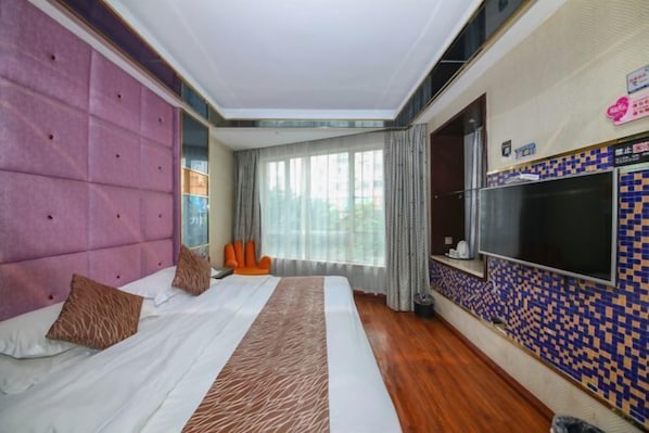 A hotel room with a large bed, a TV, and a window with curtains.