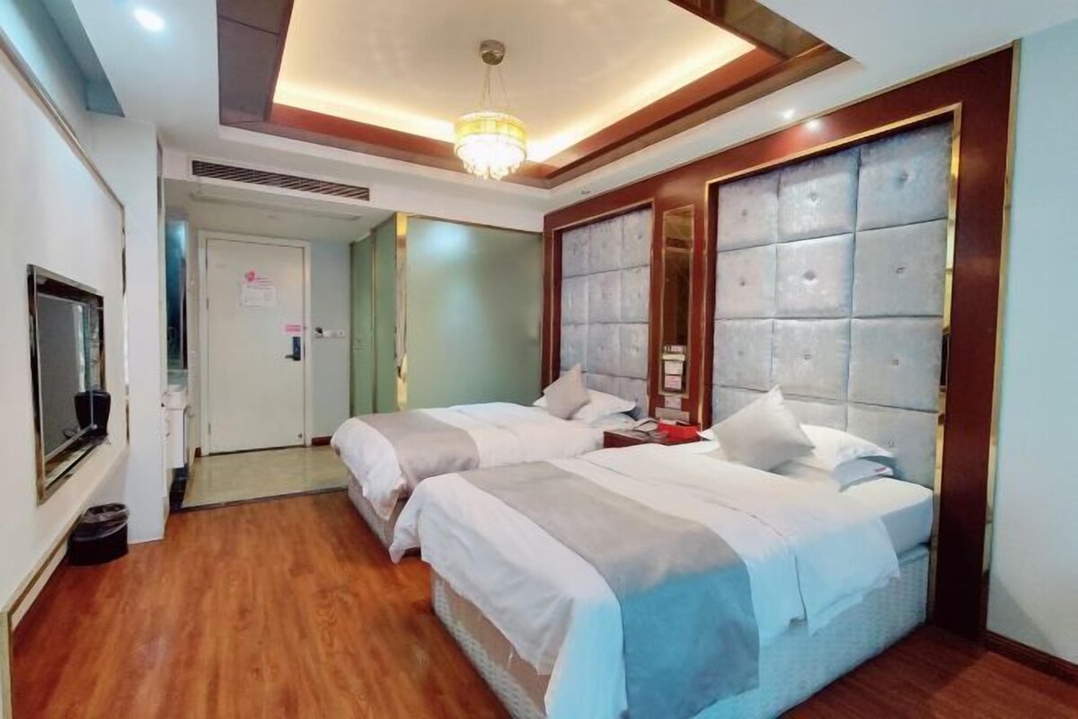 A hotel room with two beds, a large mirror, and a chandelier.
