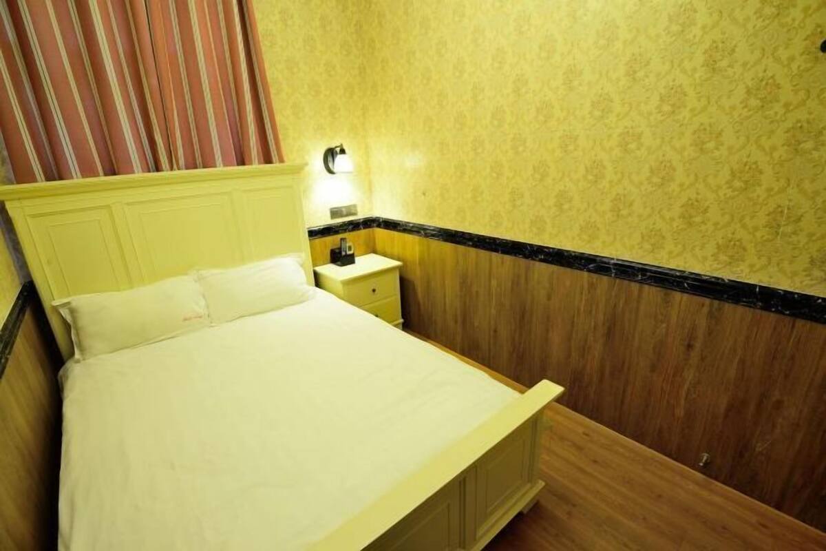 A bed with a headboard, a bedside table with a lamp, and a wall with a floral pattern.
