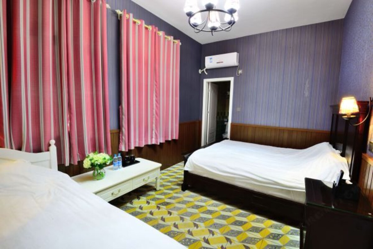A hotel room with a bed, bedside table, and a desk with a lamp.