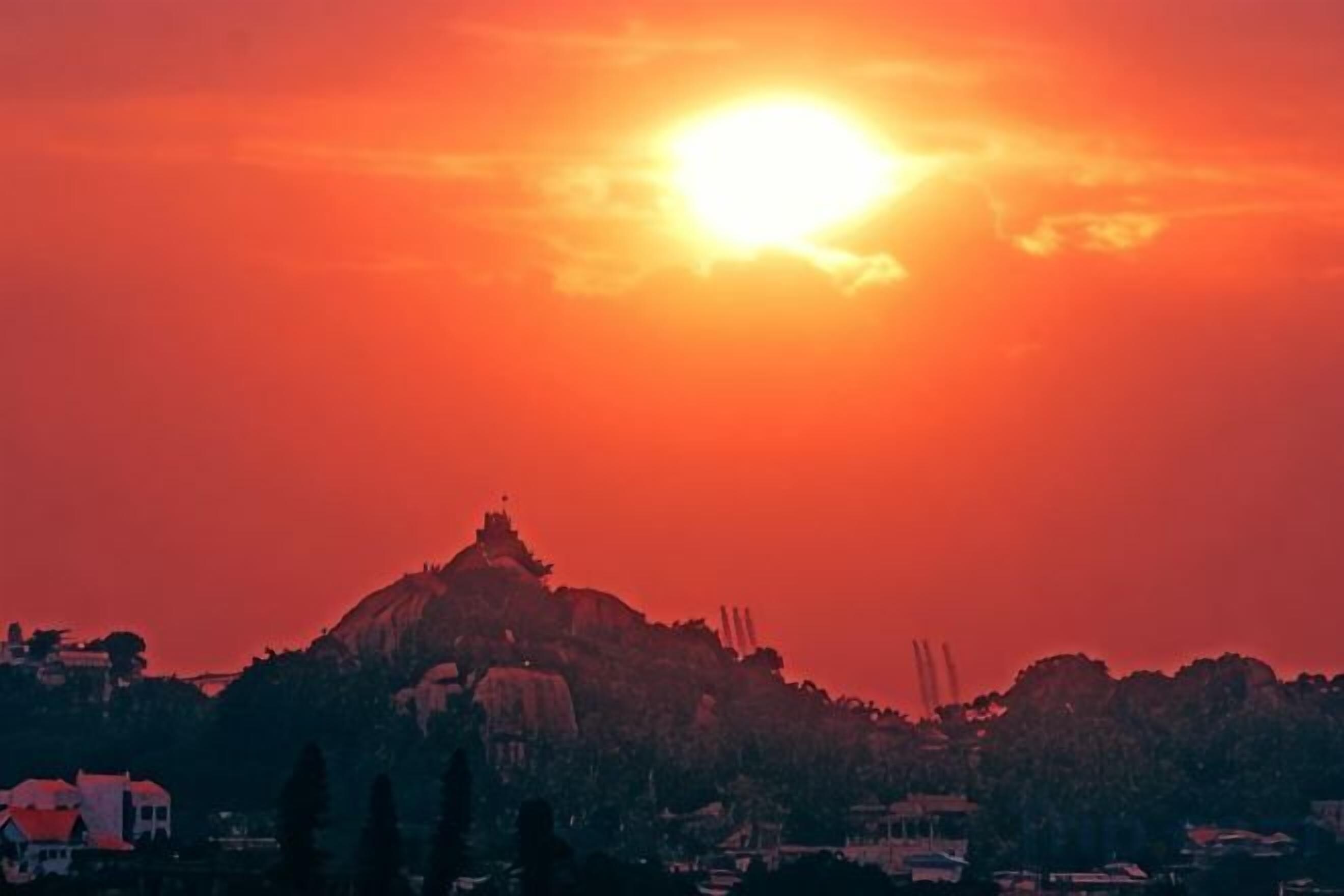 A sunset over a hill with buildings in the foreground.