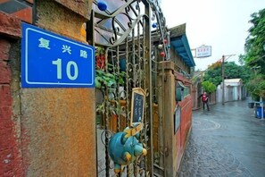 A blue sign with white text indicating a location, a metal gate with a decorative figure, and a paved pathway. - Fuxing No. 10 Hotel (Xiamen)