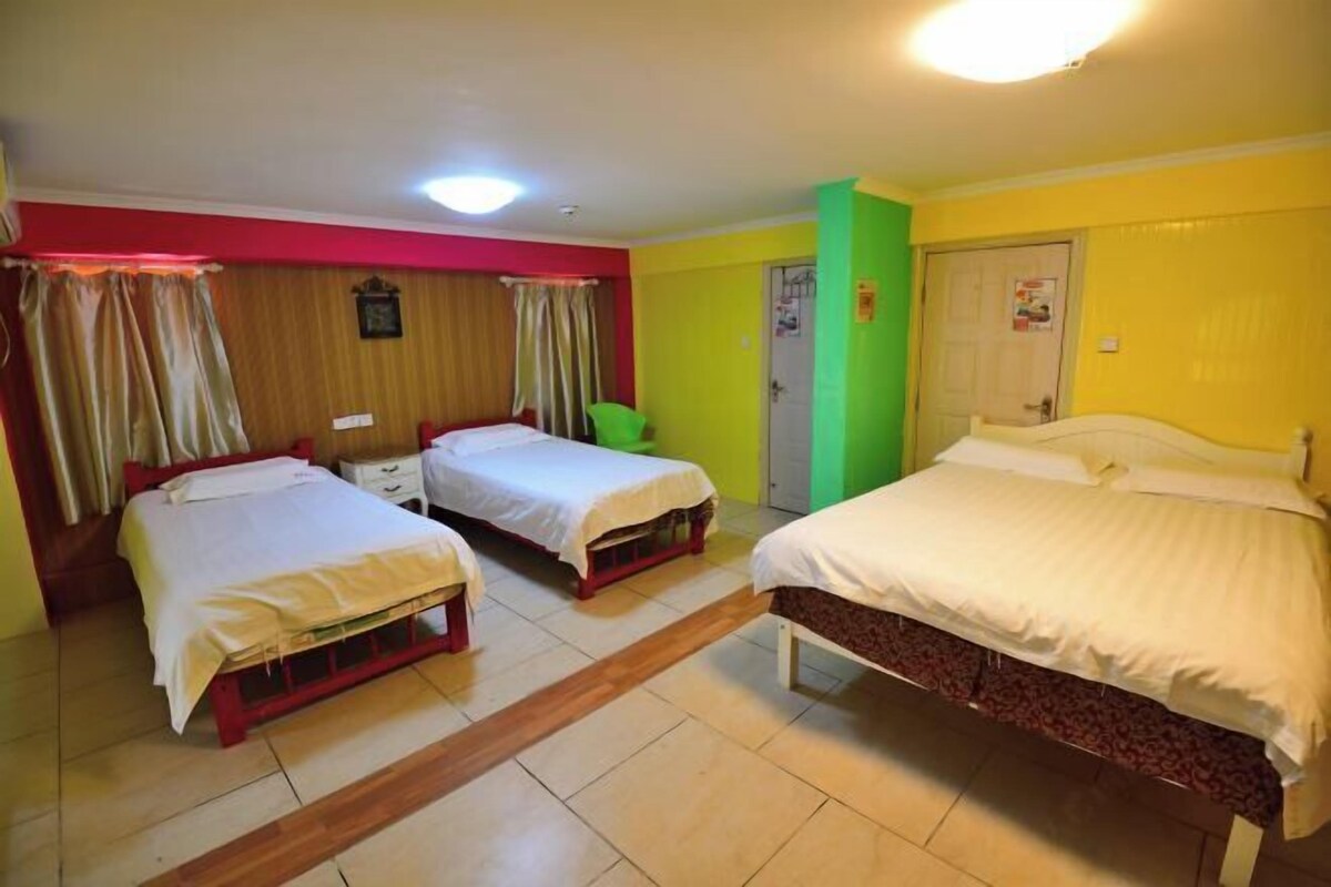 Una habitación con tres camas, piso de madera, pared verde y una puerta.
