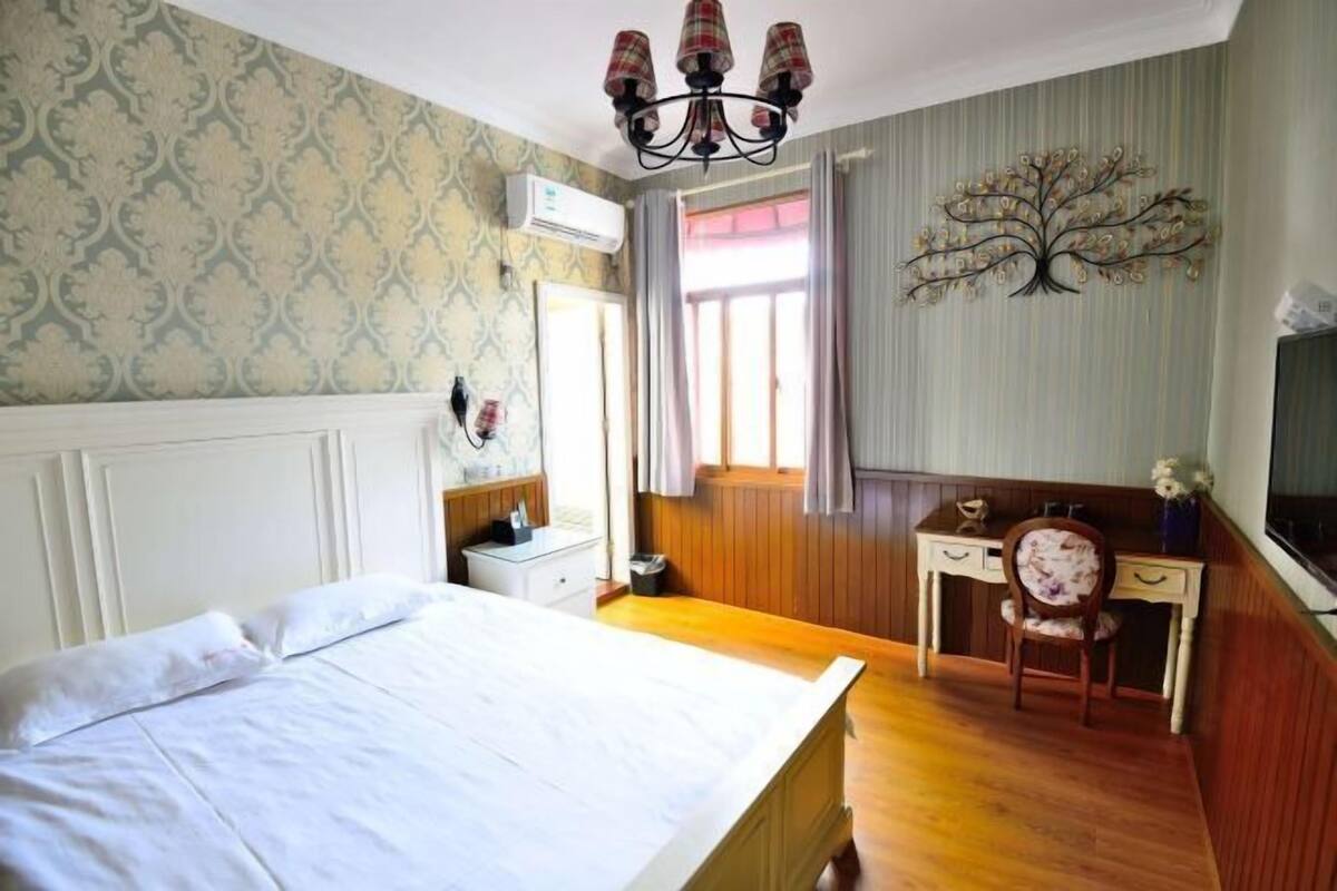 A bedroom with a bed, a desk, a chair, an air conditioning unit, and a decorative tree wall art.