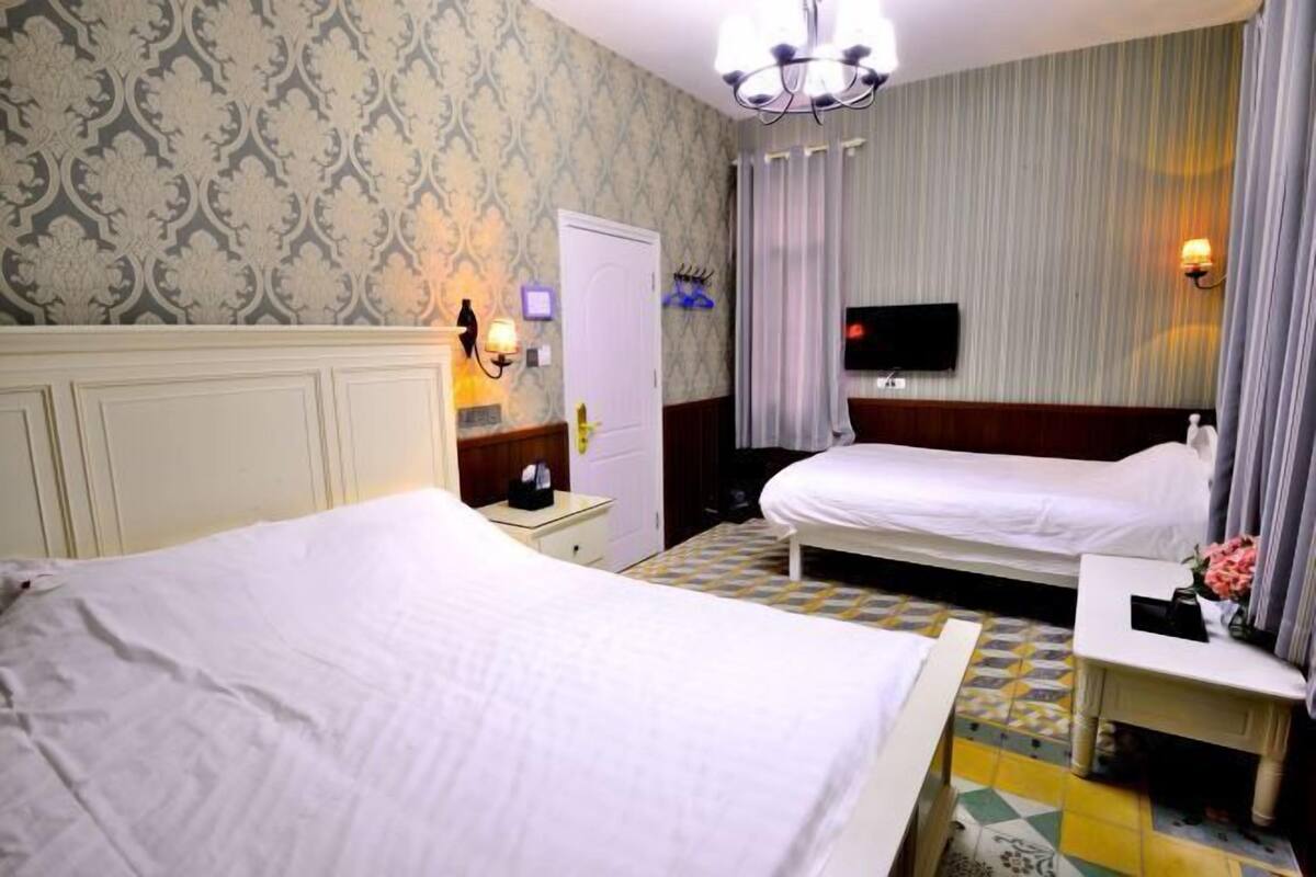 A hotel room with two beds, a television, a small table with a vase, and a patterned wallpaper.