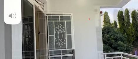 A balcony with a white railing, a glass door with decorative patterns, and two wooden stools.